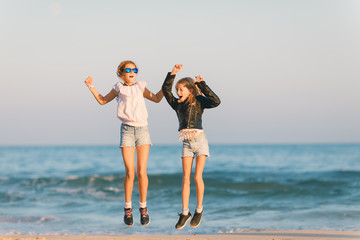 Two young girls jumping on the beach, seaside