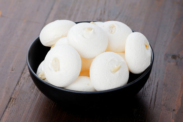 White meringues on a black plate on a wooden background. Meringues with peanuts.