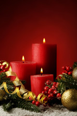 Christmas candle with fir-tree branches and baubles on red background