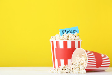 Fototapeta na wymiar Popcorn in striped buckets and paper with inscription Ticket on yellow background