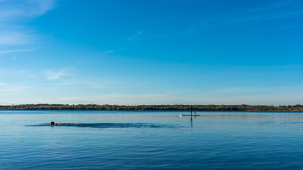 Naklejka na ściany i meble Triathlete swimming in a blue lake, sail boat far away