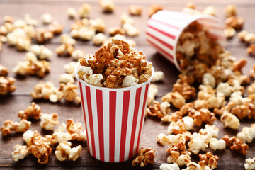 Caramel popcorn in striped cup on wooden table
