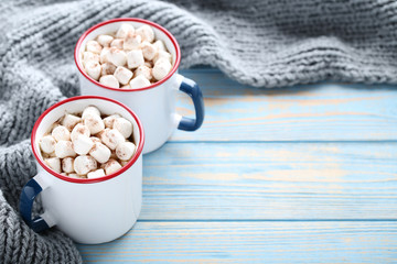 Cappuccino with marshmallows in mugs and knitted scarf on wooden table