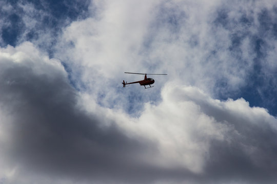 Red helicopter high in the blue sky with white clouds