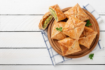 Puff pastry squares filled with potato, cheese and spinach on white wooden table.top view