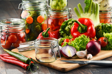 Jars with marinated food and raw vegetables on cutting board
