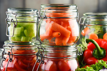 Fototapeta na wymiar Jars with marinated food and raw vegetables on cutting board