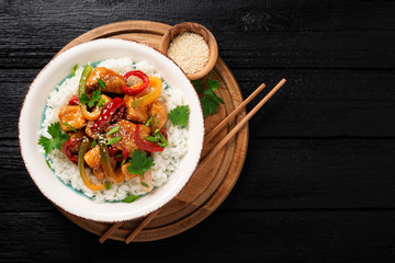 Stir-fry with chicken meat, vegetables and rice in bowl on black wooden background.
