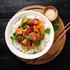 Stir-fry with chicken meat, vegetables and rice in bowl on black wooden background.