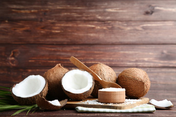 Ripe coconuts with flakes in bowl and palm leafs on brown wooden table