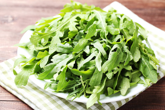 Green arugula leafs in plate with napkin on wooden table