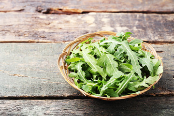 Fototapeta premium Green arugula leafs in basket on wooden table