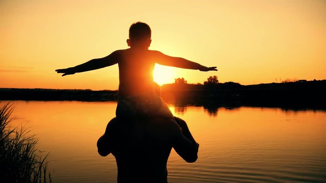 father and son silhouettes playing on beach boy rising up hands imitating a flight at wonderful sunset through the shining sun happy family concept of a united family
