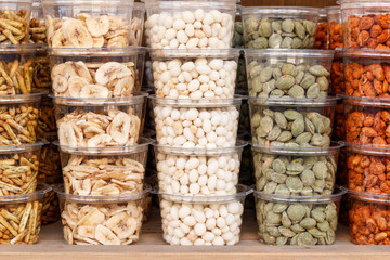 Stacked transparent plastic trays full of different kinds of nuts on the shelf of a store full of delicacies.