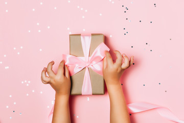 Child hands holding beautiful gift box on pink background