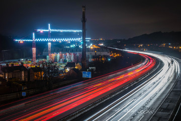 Fototapeta na wymiar Lights From Heavy Traffic On The M1 Motorway As They Snake Past Two Illuminated Cranes