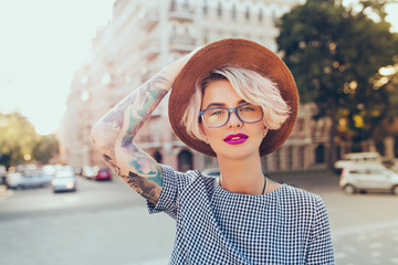 Portrait of pretty blonde girl with short hair posing to the camera on the steet in city. She wears...