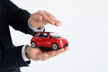 Male insurance agent holding toy car on white background, closeup. Space for text