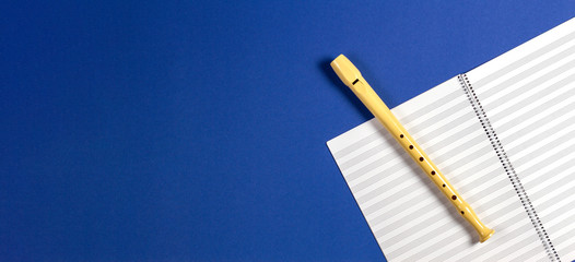 Open exercise book with pentagrams and musical instrument flute on blue background © vejaa