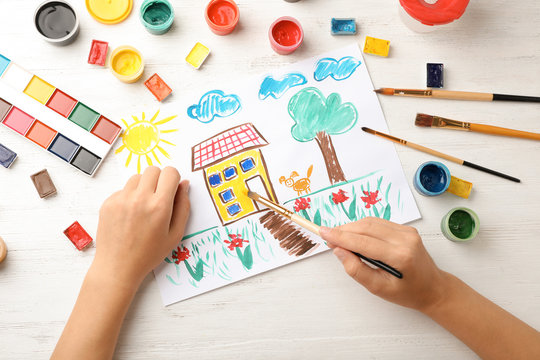 Girl painting picture of house on table, top view