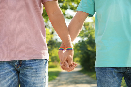Gay couple with wristbands holding hands outdoors, closeup