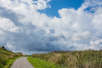 A green meadow and narrow path through it with and sky with white-grey clouds in Denmark