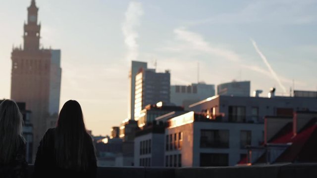 Two gitls stand on the rooftop and have a drink