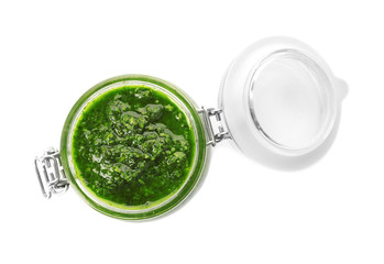 Homemade basil pesto sauce in glass jar on white background, top view