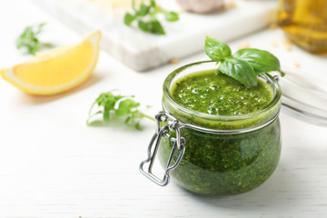 Homemade basil pesto sauce in glass jar on table - obrazy, fototapety, plakaty
