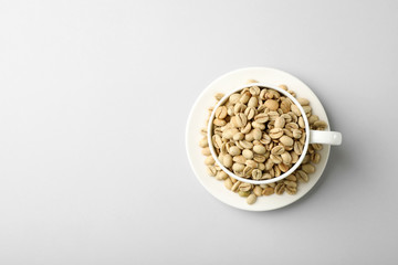 Cup and saucer with green coffee beans on white background, top view. Space for text