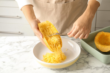 Woman scraping flesh of cooked spaghetti squash with fork in kitchen