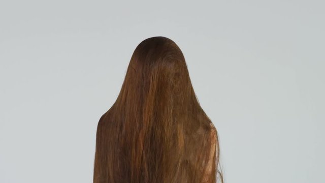 Slow motion shot of a woman letting her very long brown hair go over her head. 