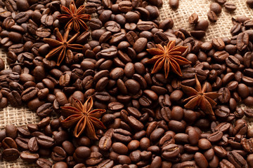Sackcloth covered with coffee beans with anise stars. Atmospheric background for coffee printing. Cover or background for a coffee menu. High angle of a cafe theme.