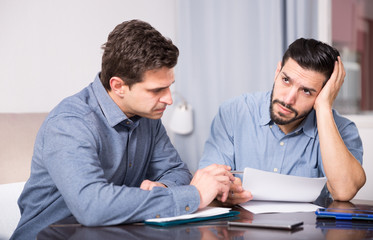 Two troubled men reading documents at desk