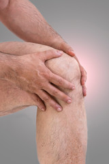 Fototapeta premium Man suffering from knee pain.A mature man massaging his painful knee, suffering from painful knee joint on grey from frofile