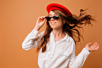 Attractive young stylish woman wearing red hat and white shirt posing on isolated background with flying hair at camera, place for text, true emotions
