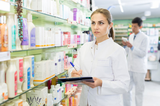Female pharmacist checking medicine with notebook in  drugstore