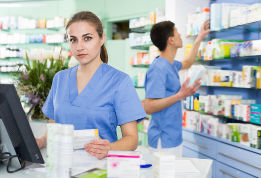 Adult pharmacist is standing near cashbox