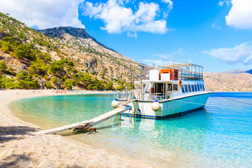 Tourist boat anchoring at beautiful Apella beach on Karpathos island, Greece - obrazy, fototapety, plakaty