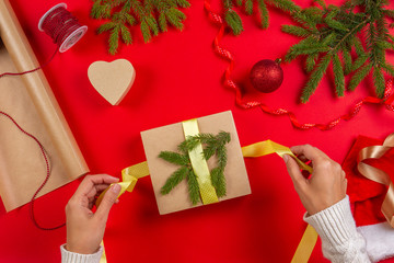 Christmas gift wrapping. Woman's hands packing Christmas present box on red table background