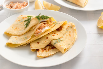 Crepes filled with dill, cream cheese and smoked salmon on white plate.