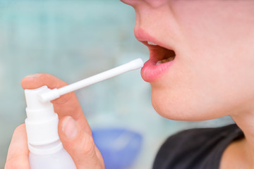 woman using spray from the pain in her throat. treatment of colds, flu