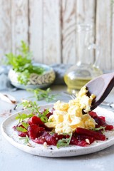 Scramble of eggs with carpaccio of baked beets with walnuts, aromatic herbs and arugula on a plate. Delicious healthy breakfast.  Beet carpaccio with sauce on a white plate.