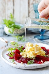 Scramble of eggs with carpaccio of baked beets with walnuts, aromatic herbs and arugula on a plate. Delicious healthy breakfast.  Beet carpaccio with sauce on a white plate.