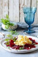 Scramble of eggs with carpaccio of baked beets with walnuts, aromatic herbs and arugula on a plate. Delicious healthy breakfast.  Beet carpaccio with sauce on a white plate.