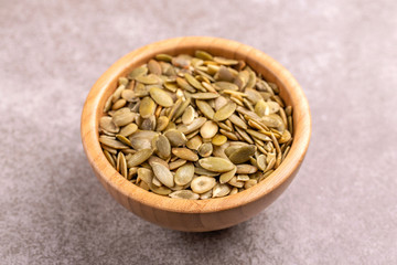 Fresh pumpkin seeds in wooden bowl on marble background