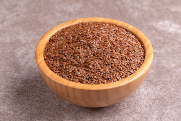 Raw flax seeds in wooden bowl on gray marble background.