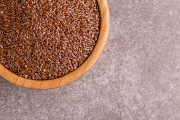Raw flax seeds in wooden bowl on gray marble background.