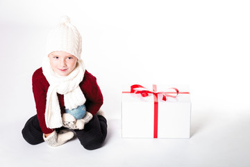 Merry Christmas and happy New year! Cute happy little boy with present and toy. Kid enjoy holiday in warm clothes. Portrait kid on light background isolated. Happy Child sitting with place for text