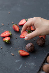 Woman hand hold slice of strawberry, chocolate candy's near at black background